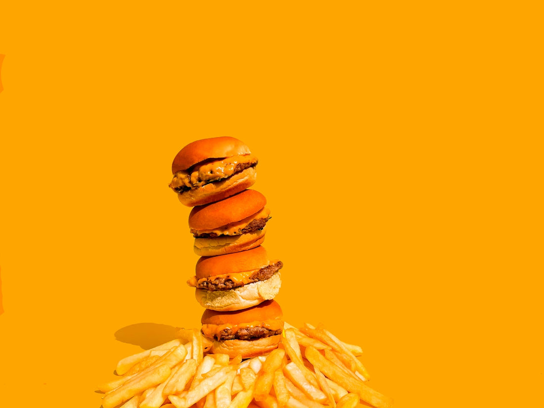 a stack of hamburgers and french fries on a yellow background