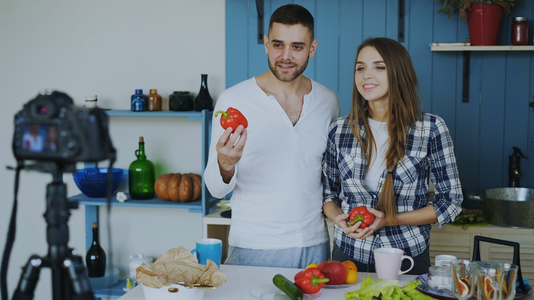 Couple holding red bell peppers in a kitchen.